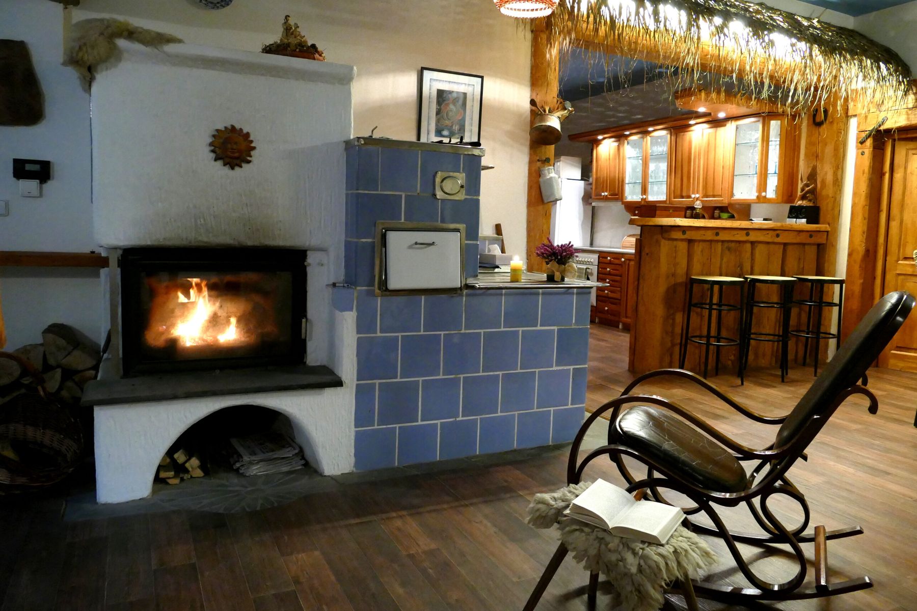 Kachlová kamna s modrými kachlemi a hořícím krbem, v pozadí bar