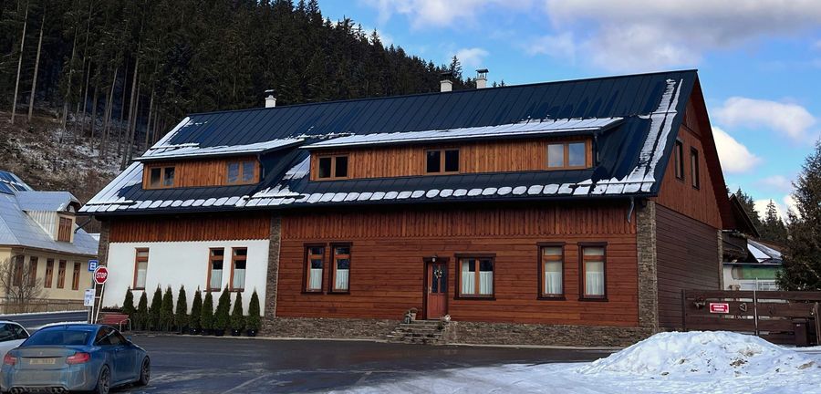 Chalupa zepředu se zasněženou střechou a parkováním u domu